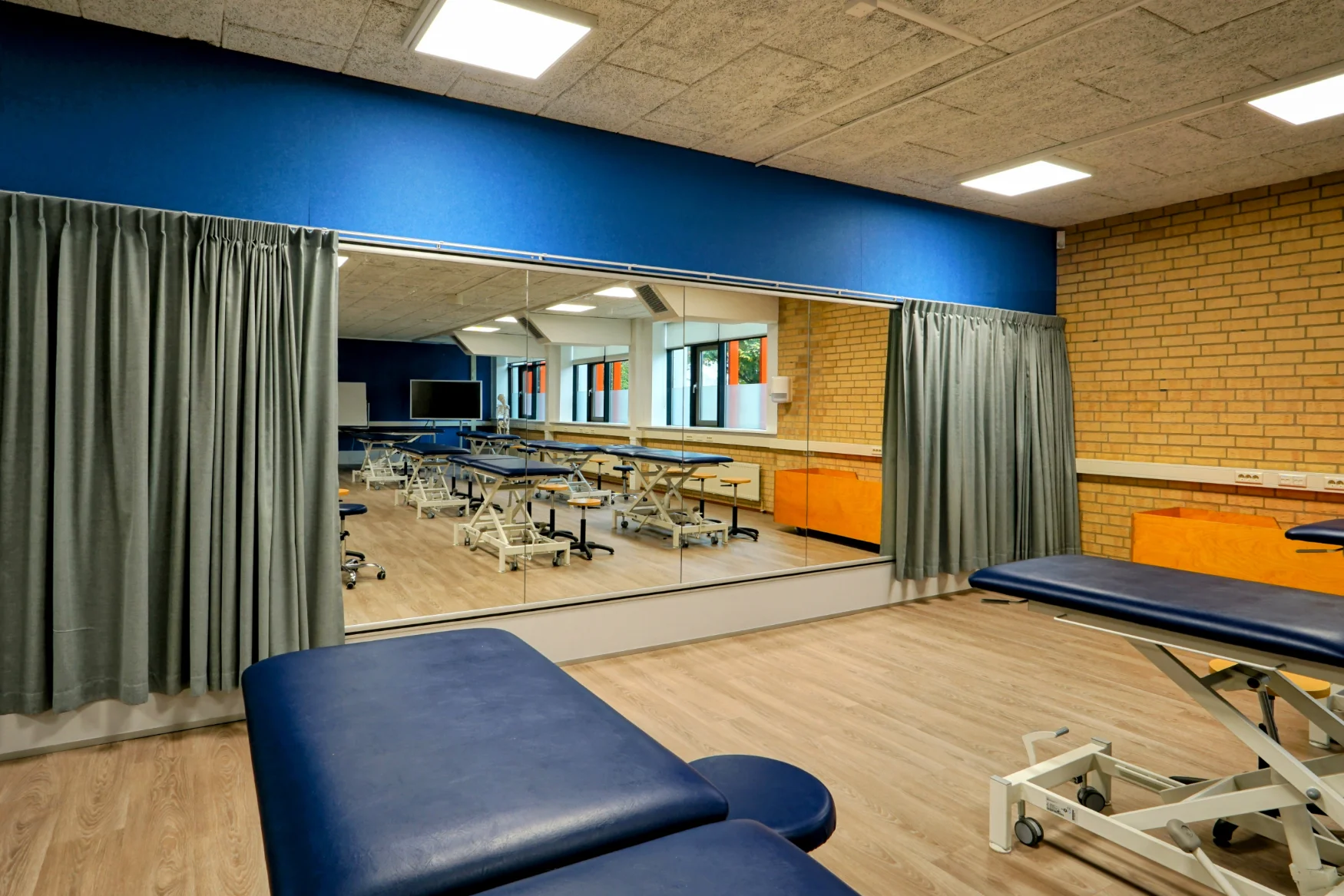 Akoestische wandbekleding met blauwe PET acoustic panels en geïntegreerde oefenspiegels in een onderwijsruimte, gerealiseerd door Blossom Interior (Blossom Architecture).