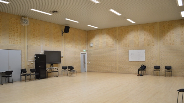 Oorspronkelijke gymzaal Windesheim vóór transformatie – bakstenen wanden, houten sportvloer en losse audiovisuele apparatuur